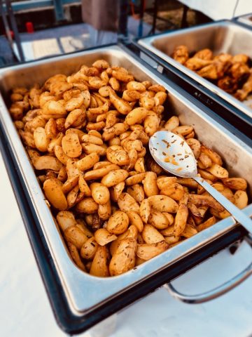 Gewürzte Bratkartoffeln in Metallwanne auf Marktstand.