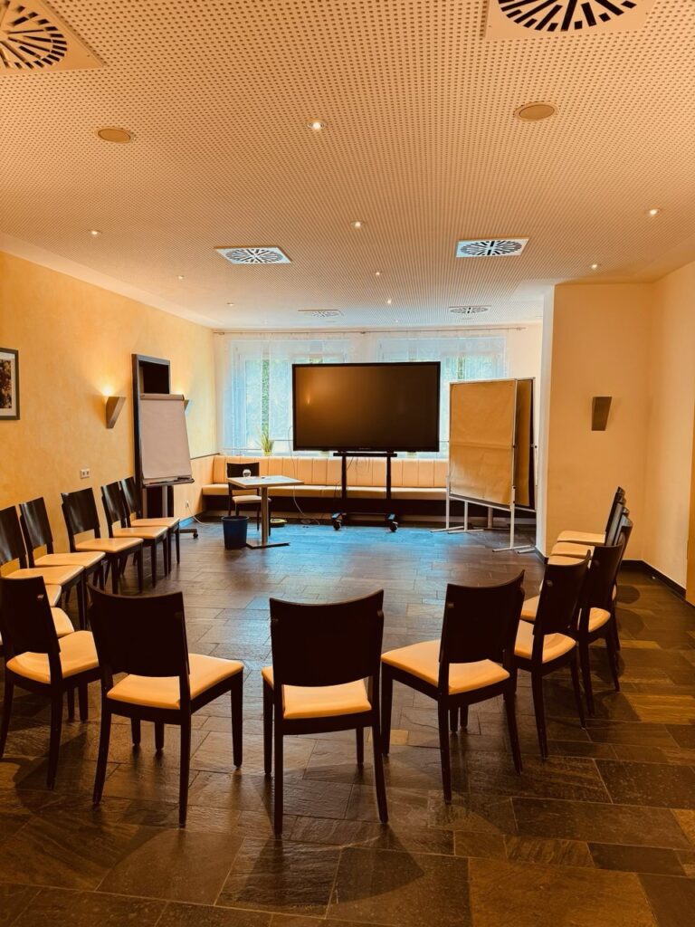 Konferenzraum mit Stühlen und Präsentationsbildschirm.